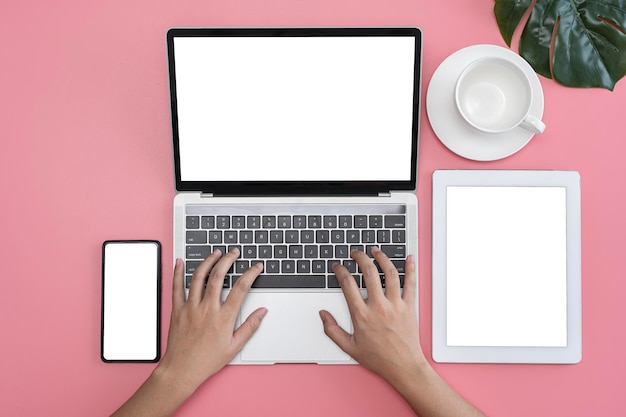 Vista superior del escritorio rosa pastel Manos de mujer usando un teléfono inteligente portátil y una taza de café con pantalla de tableta Espacio en blanco