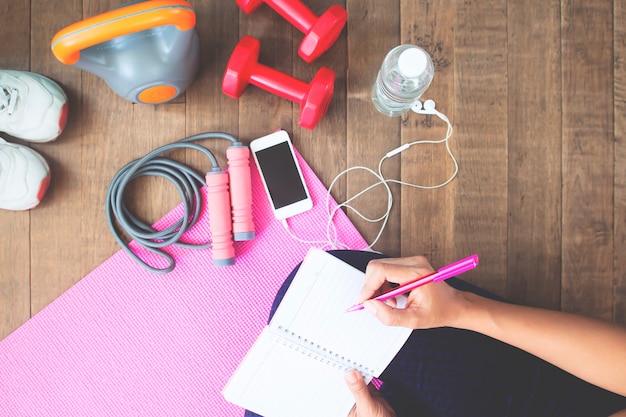 Foto vista superior de la escritura deportiva de la mujer en el cuaderno, planeando entrenamiento