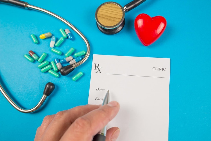 Foto vista superior de la escritura a mano de un médico que escribe una receta un estetoscopio y un corazón rojo también están sobre un fondo azul