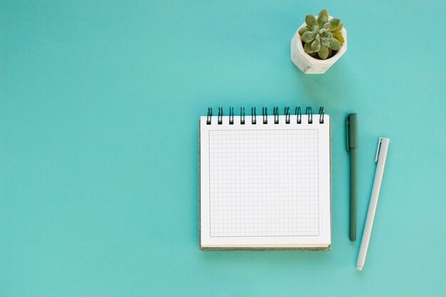 Vista superior del espacio de trabajo y cuaderno abierto con páginas en blanco simuladas sobre fondo azul Plano