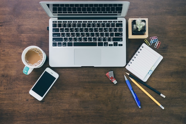 Vista superior del espacio de trabajo del escritorio de oficina con taza de café, computadora portátil, teléfono inteligente y teclado