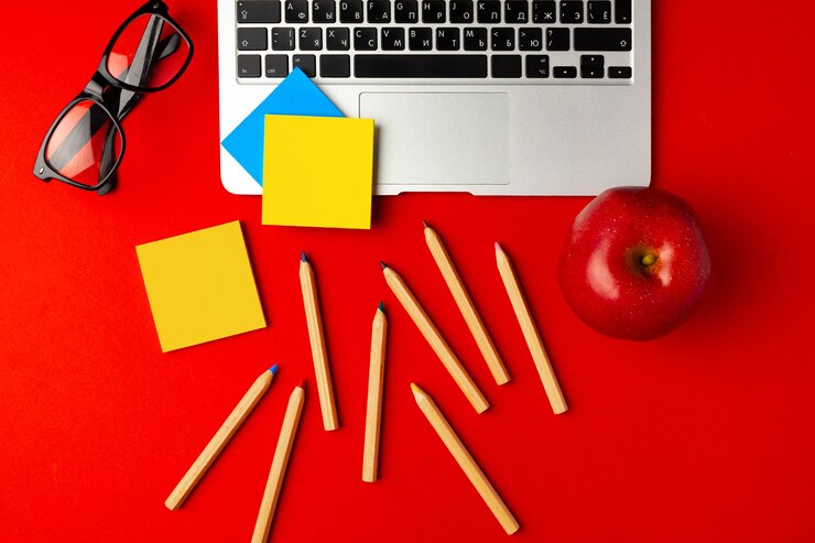 Foto vista superior del espacio de trabajo del estudiante con computadora portátil abierta y manzana roja, otros suministros