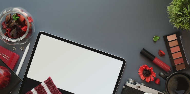 Foto vista superior del espacio de trabajo femenino de lujo rojo con tableta sobre fondo de escritorio gris oscuro con maquillaje y útiles de oficina