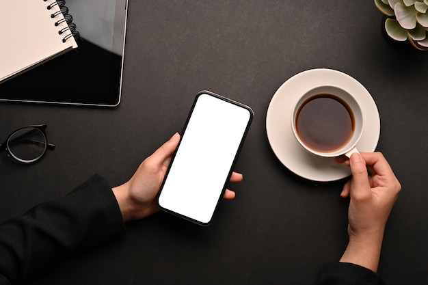 Vista superior Espacio de trabajo con manos femeninas usando un teléfono inteligente y sosteniendo una taza de café
