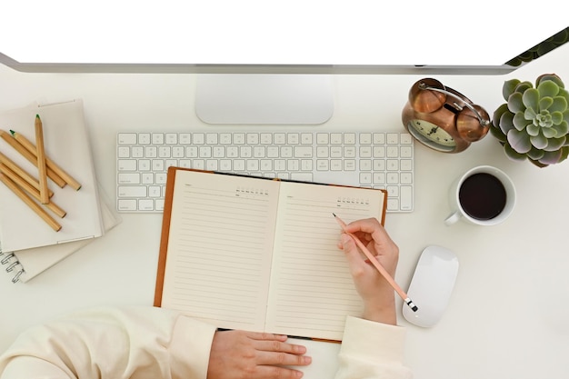 Vista superior de un espacio de trabajo moderno con la mano de una mujer escribiendo algo en su cuaderno o diario