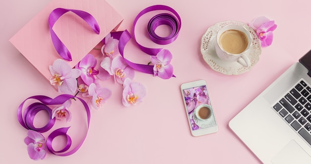 Vista superior del espacio de trabajo de la oficina en casa rosa con computadora portátil, teléfono y taza de café. Plano de redes sociales con café, flores y teléfono inteligente. Lugar de trabajo floral rosa femenino