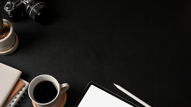 Vista superior del espacio de trabajo con tableta, portátil, cámara, taza de café y espacio de copia en la mesa negra