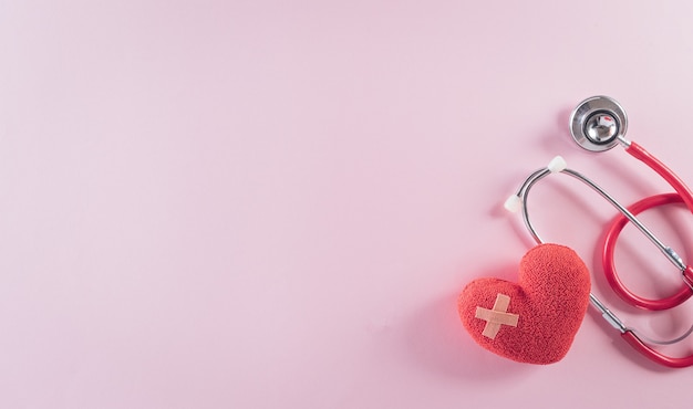 Vista superior del estetoscopio médico y corazón rojo sobre fondo rosa