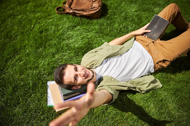 Vista superior de un estudiante masculino alegre con una tableta en sus manos mirando hacia arriba