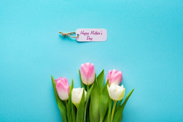 Vista superior de la etiqueta de papel con letras del día de la madre feliz y tulipanes sobre fondo azul