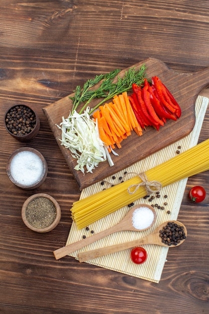 Vista superior fatiada de legumes, repolho, cenoura, verduras e pimenta na superfície da tábua de cortar marrom