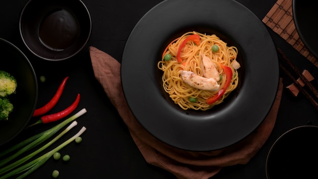 Foto vista superior de fideos schezwan o chow mein con vegetales y pollo servido en plato negro