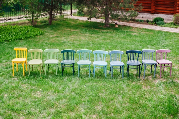 Vista superior de una fila de sillas vienesas de madera pintadas en alegres colores brillantes en el patio trasero