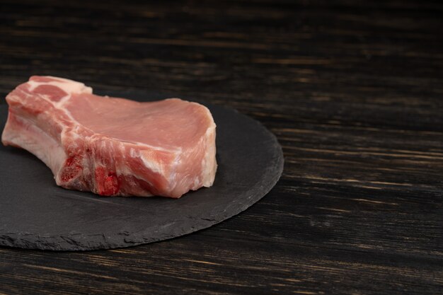 Vista superior de filetes de chuleta de cerdo cruda de una pieza sobre una tabla de cortar de piedra negra.