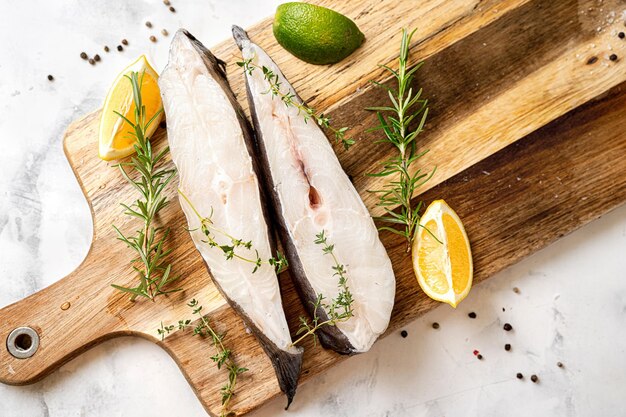 Vista superior de filetes de pescado halibut fresco y crudo con hierbas y limón en una tabla de madera