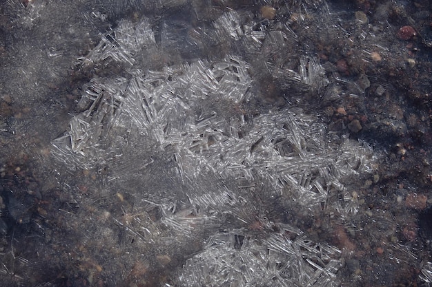 Vista superior de la fina capa de hielo que cubre la superficie del charco en suelo pedregoso en el frío día de invierno en el campo