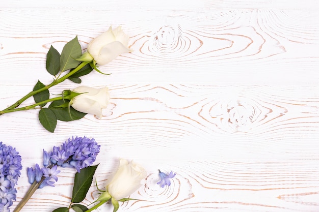 Vista superior de flores de jacinto azul y rosas blancas sobre una mesa de madera blanca