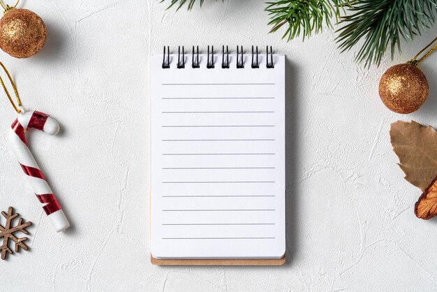 Vista superior del fondo de adornos navideños con cuaderno en blanco sobre fondo blanco de mesa con espacio de copia, concepto de celebración navideña.