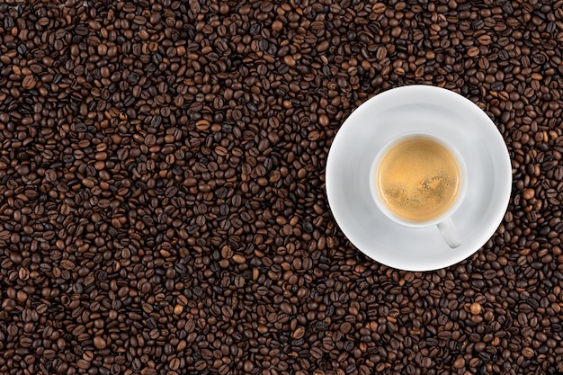 Vista superior del fondo de los aromáticos granos de café marrón y una taza de espresso