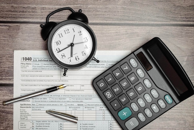 Vista superior del formulario de impuestos 1040 con calculadora de pluma y reloj despertador negro documento financiero de tiempo de impuestos