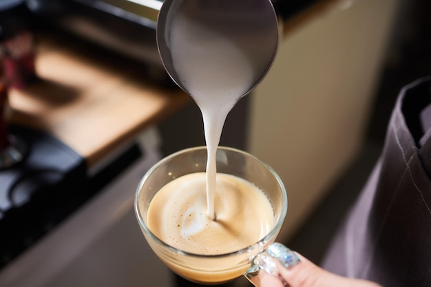 Vista superior de la foto de barista profesional vertiendo leche del frasco en una taza de café que se está preparando