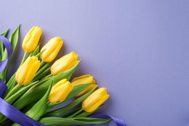 Vista superior de la foto de la composición del día de la mujer ramo de tulipanes amarillos y cinta morada sobre fondo lila pastel aislado con espacio vacío