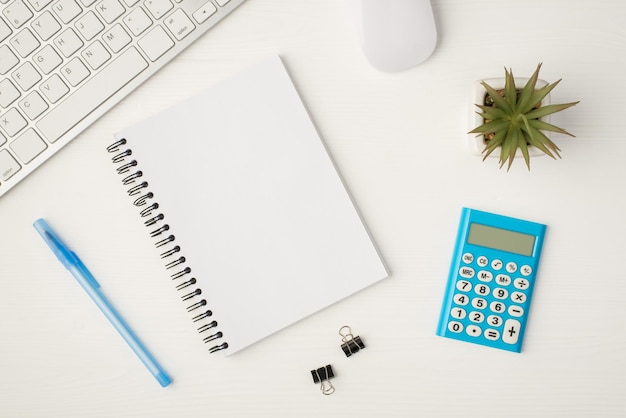 Vista superior de la foto del lugar de trabajo de negocios con teclado, ratón, carpetas de plantas, cuaderno con calculadora azul copyspace y bolígrafo sobre fondo blanco aislado