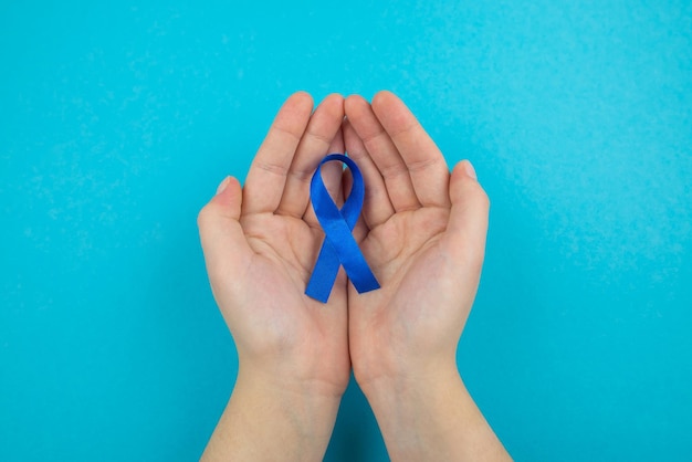 Vista superior foto en primera persona de manos femeninas sosteniendo cinta azul en las palmas símbolo de conciencia de cáncer de próstata en azul pastel aislado