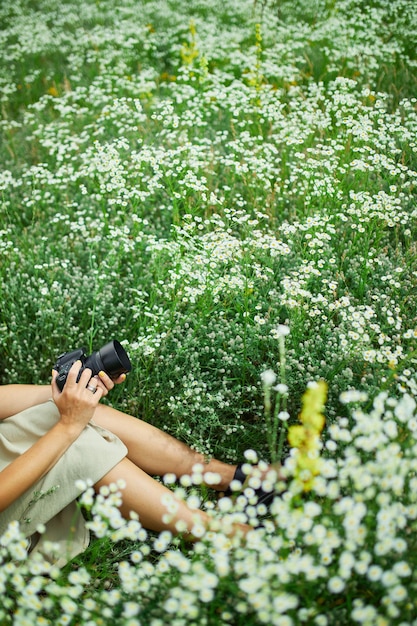 Vista superior de la fotógrafa sentada al aire libre en el paisaje de campo de flores sosteniendo una cámara