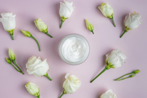 Foto vista superior de un frasco abierto con cara abarrotada rodeada de flores de eustoma en flor esparcidas presentación de cosméticos para el cuidado de la piel