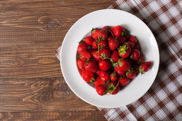 Vista superior de fresas maduras frescas en el plato blanco que se encuentra en la mesa de madera vieja