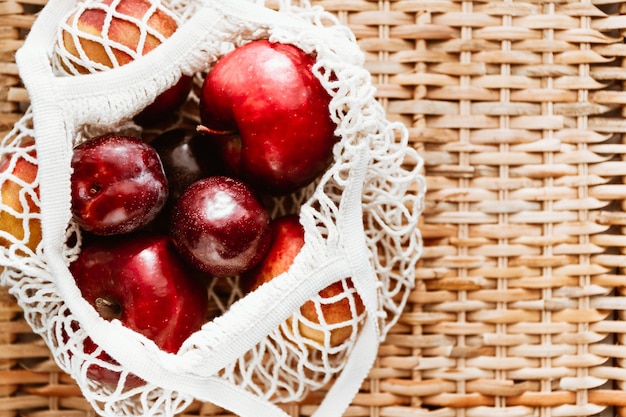 Vista superior de frutas en una bolsa de red ecológica sobre fondo de ratán