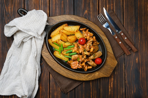 Vista superior de gajos de papa con rebozuelos y carne de cerdo en sartén de hierro fundido