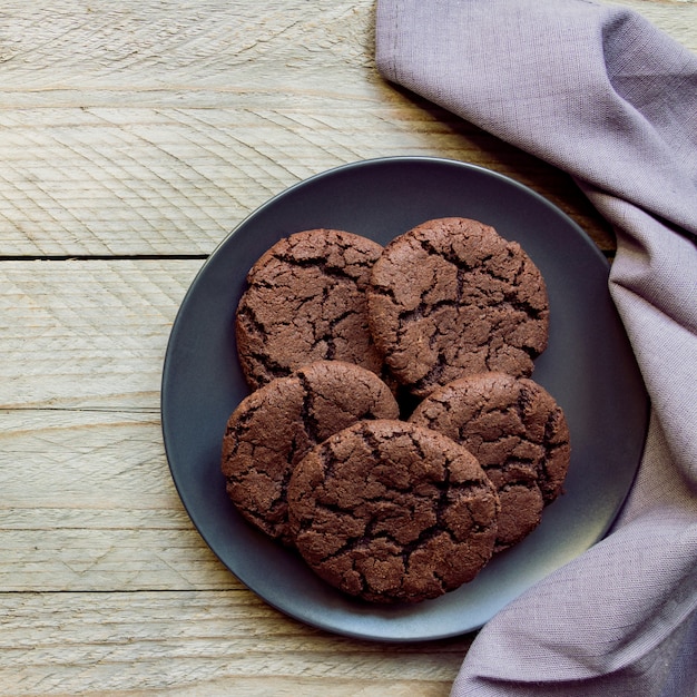 Vista superior, galletas de chispas de chocolate en un plato negro. Fondo de madera. Desde arriba.