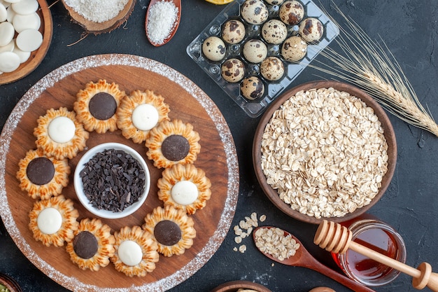 Vista superior de galletas con chocolate y chocolate negro sobre tablero de madera cuencos con avena dulces huevos de codorniz en tarro de miel viol en la mesa