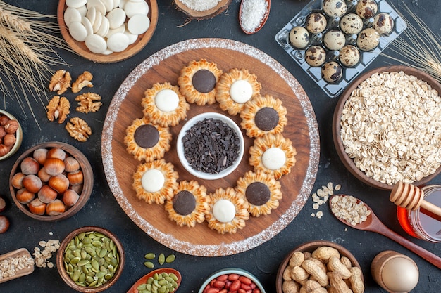 Vista superior de galletas con chocolate y chocolate negro sobre tablero de madera cuencos con nueces avena dulces huevos de codorniz en viol tarro de miel en la mesa