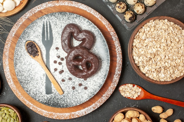 Vista superior galletas con horquilla de chocolate impresión con azúcar glas cuchara de madera en un plato avena nueces en cuencos huevos de codorniz en viola en la mesa