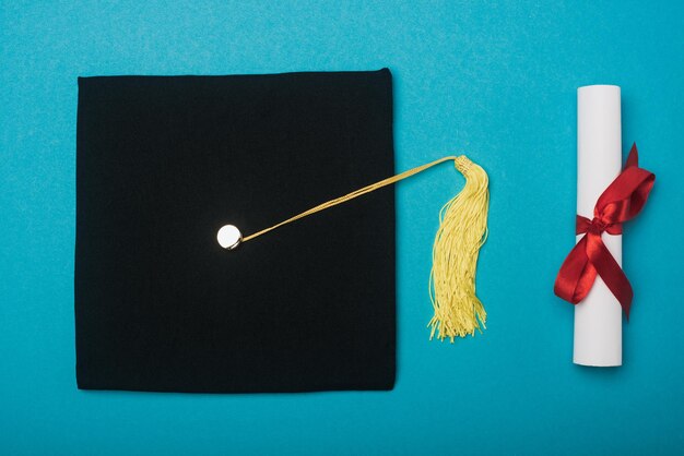 Vista superior de la gorra de graduación negra con borla amarilla y diploma sobre fondo azul