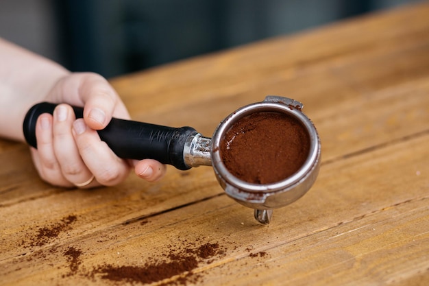 Vista superior de granos de café en filtro sin fondo con taza de café negra en la mesa de madera Enfoque selectivo Granos de café en un filtro sin fondo en una mesa de madera