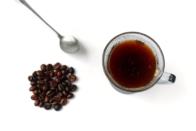 Vista superior de los granos de café con una taza de café y una cuchara, aislado sobre fondo blanco.