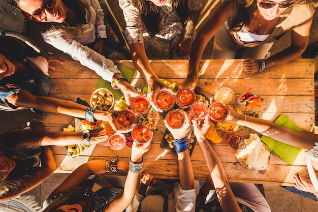 Vista superior del grupo de amigos, la gente disfruta de la comida y las bebidas brindando y tintineando con copas de vino tinto, todos juntos. divertida