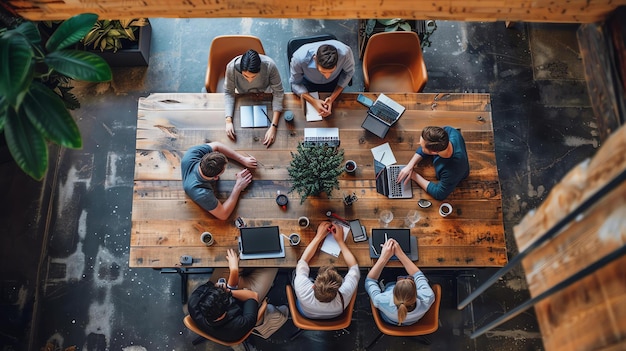 Vista superior de un grupo diverso de profesionales de negocios teniendo una reunión alrededor de una gran mesa de madera en un espacio de oficina moderno