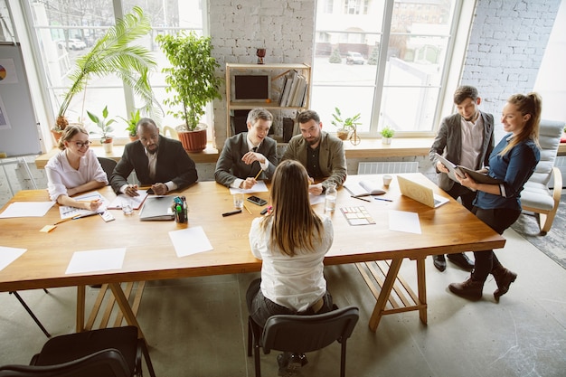 Vista superior. Grupo de jóvenes empresarios que tienen una reunión. Grupo diverso de compañeros de trabajo discuten nuevas decisiones, planes, resultados, estrategia. Creatividad, lugar de trabajo, negocios, finanzas, trabajo en equipo.