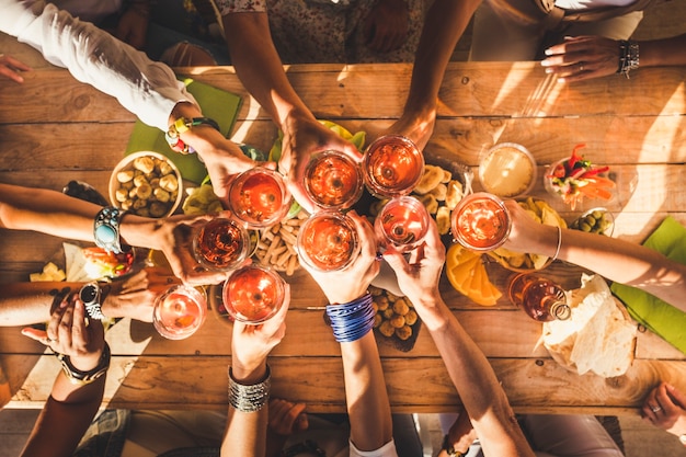 Vista superior del grupo de mujeres que tintinean y se juntan con vino tinto y mesa llena de comida - concepto de amistad y celebración