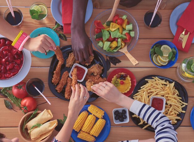 Vista superior del grupo de personas cenando juntos mientras están sentados en la mesa de madera Comida en la mesa La gente come comida rápida