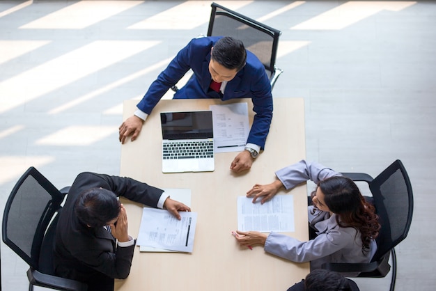 Vista superior del grupo de personas ocupadas multiétnicas que trabajan en una oficina, vista aérea con el empresario y la empresaria sentados alrededor de una mesa de conferencias con copia en blanco, reunión de negocios