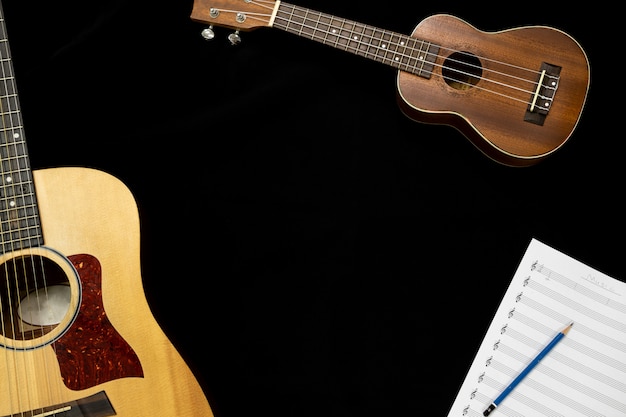 Vista superior de la guitarra y el ukelele con una hoja de notas musicales sobre el fondo negro