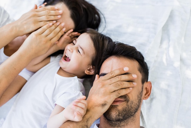 Vista superior de la hermosa familia madre bonita padre guapo y niño lindo jugando al aire libre en el parque Retrato horizontal de los ojos cerrados femeninos y masculinos con la mano jugar peek a boo con el niño Crianza de los hijos