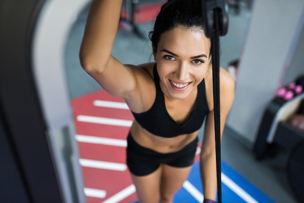 Vista superior de la hermosa mujer morena de sonrisa caucásica está haciendo ejercicios con la barra en el gimnasio mujer deportiva haciendo ejercicio con barra en el gimnasio culturismo personas y concepto deportivo