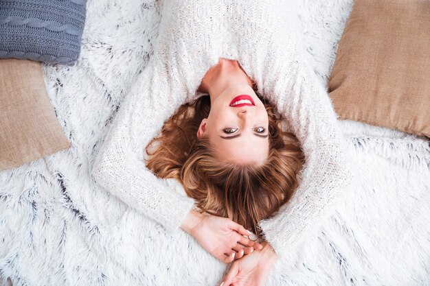 Vista superior de una hermosa mujer sonriente con suéter y lápiz labial rojo tirado en la alfombra